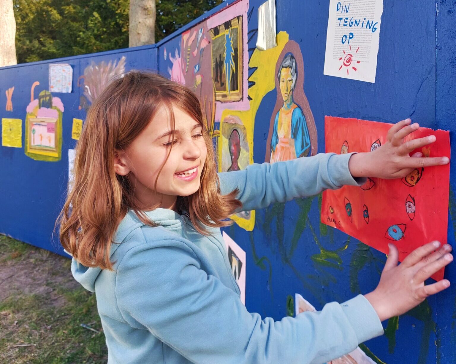 Et barn sætter sin tegning op på et blåt stakit